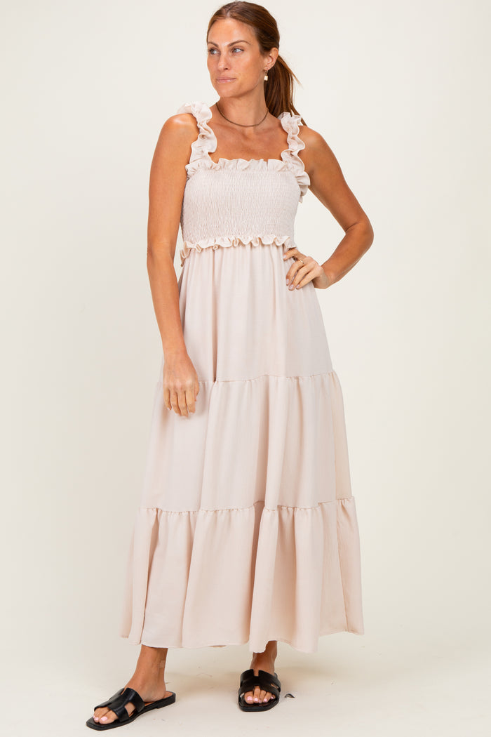 woman wearing a light beige maxi dress with ruffle straps and a smocked top, standing against a plain background
