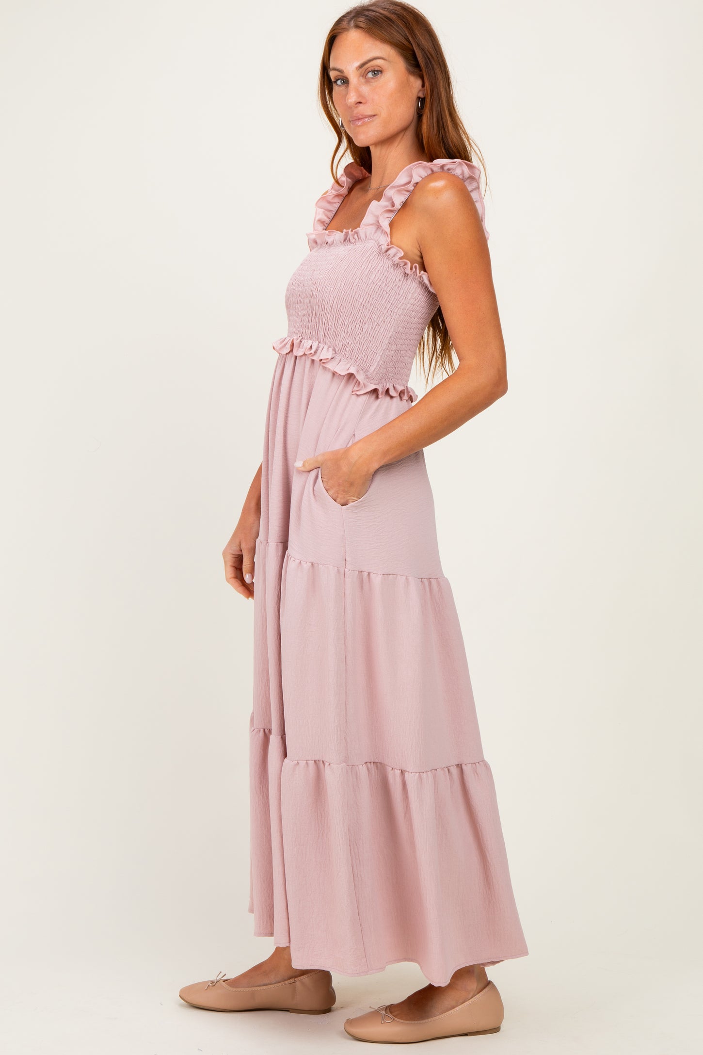 woman wearing a pink tiered maxi dress with ruffled straps and pockets, standing in profile