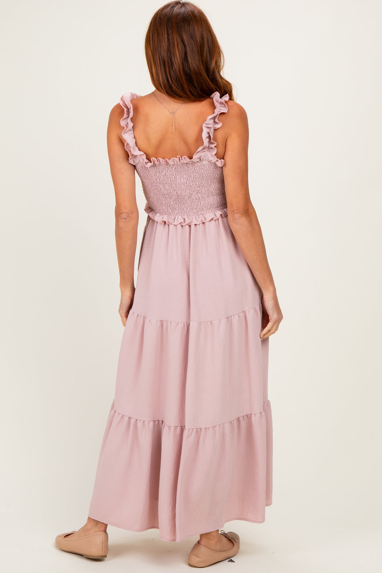 woman wearing a light pink maxi dress with ruffled straps and a smocked bodice, showing a tiered skirt from the back