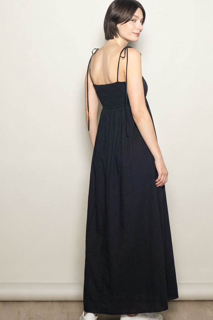 woman wearing a black maxi dress with adjustable straps and a smocked bodice, shown from the back