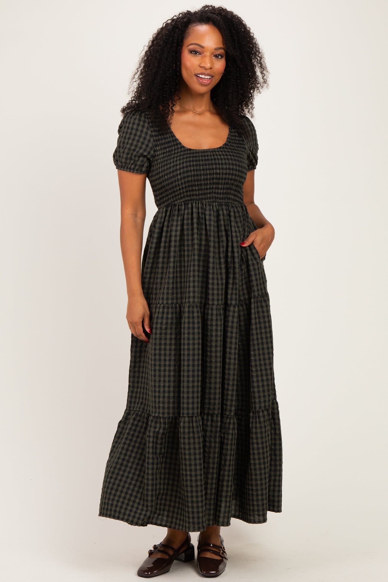 woman wearing a black and green gingham maxi dress with short puff sleeves and a tiered skirt, standing with hands in pockets