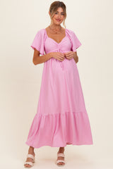 woman wearing a pink maternity maxi dress with short sleeves and gathered detail at the bust, showcasing her baby bump