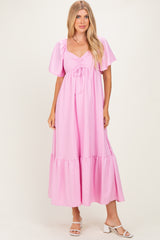 woman wearing a pink maxi dress with puff sleeves and a tie detail at the bust, standing in a light background.