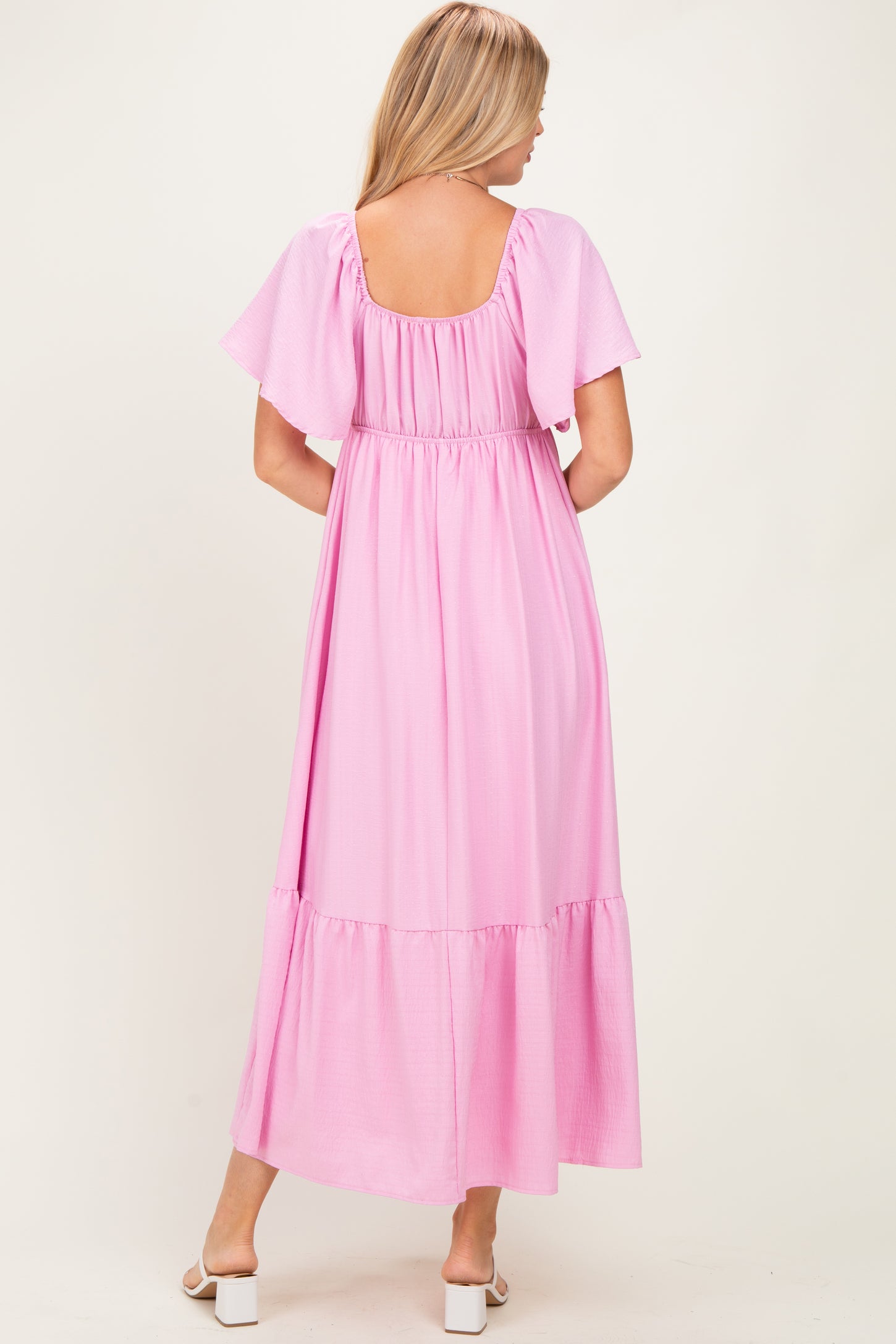 woman wearing a pink maxi dress with flutter sleeves and a tiered hem, shown from the back