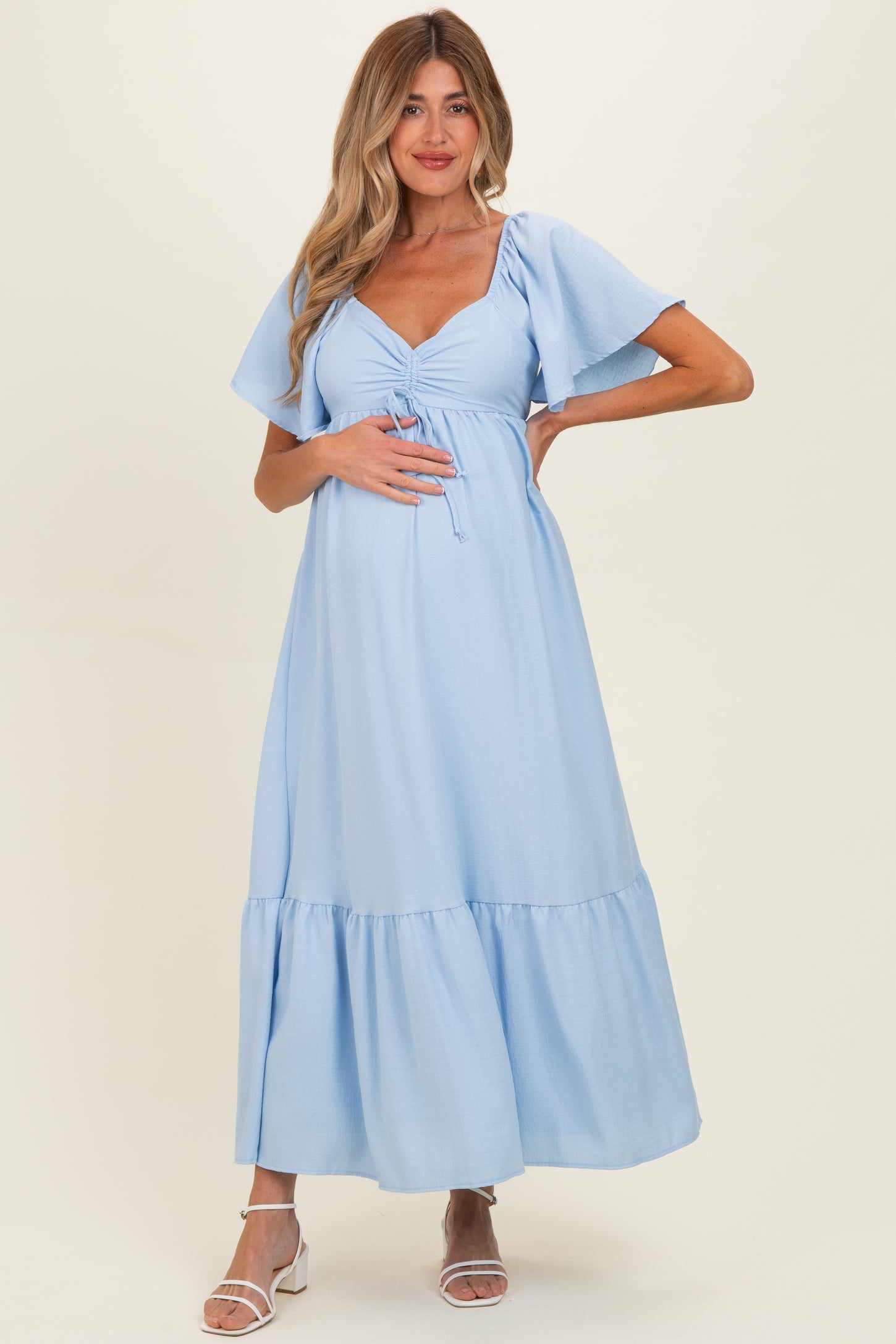 woman wearing a light blue maternity dress with flutter sleeves and a tie front, showing her baby bump