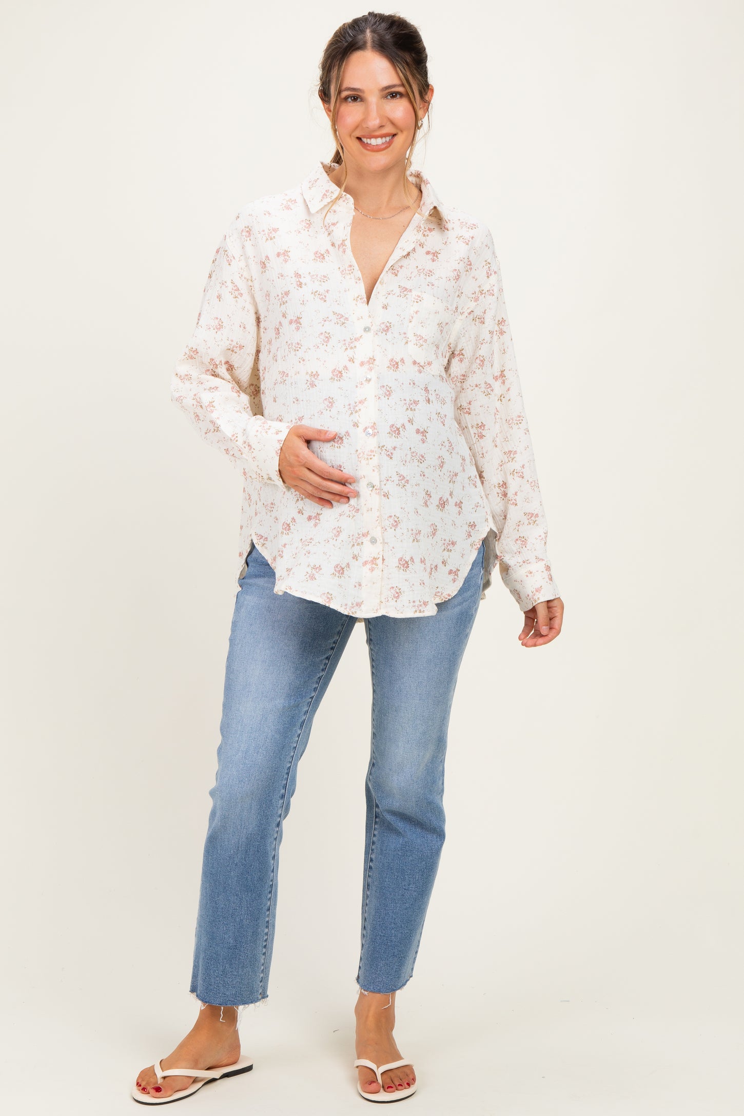 woman wearing a floral print maternity shirt and light blue jeans, gently holding her baby bump