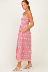 woman wearing a pink striped maxi dress with floral embroidery and pockets, paired with white strappy sandals