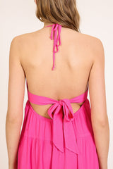 woman wearing a bright pink halter dress with an open back and a tie detail at the waist