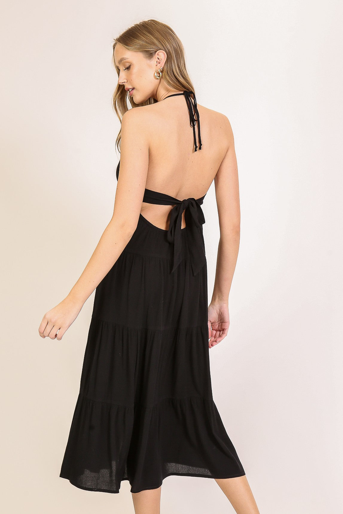 woman wearing a black halter neck tiered dress with an open back and a tied detail at the waist