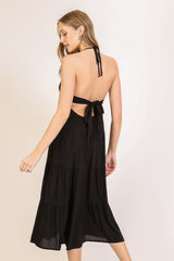 woman wearing a black halter neck tiered dress with an open back and a tied detail at the waist