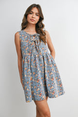 woman wearing a blue floral sleeveless mini dress with a lace-up neckline and a gathered waist