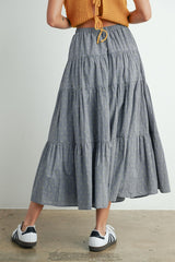 woman wearing a gray tiered maxi skirt with a lightweight fabric and paired with white and black sneakers