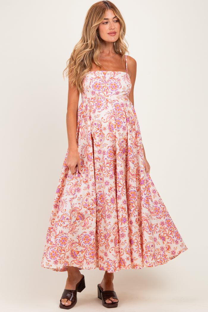 woman wearing a pink and white floral maternity dress with spaghetti straps and a flowy skirt, showing her baby bump