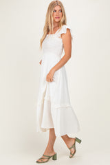 woman wearing a white midi dress with ruffled sleeves and a smocked bodice, standing sideways
