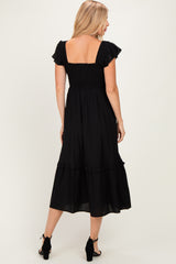 woman wearing a black smocked back maxi dress with ruffle details on sleeves and hem, seen from the back