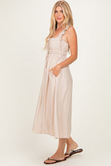 woman wearing a beige midi dress with adjustable straps and side pockets, standing sideways and wearing flip-flops