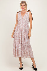 woman wearing a light pink sleeveless maxi dress with a tiered skirt and bow tie straps