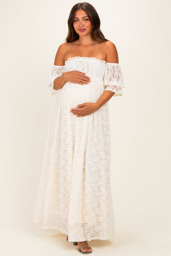 woman wearing a white off-the-shoulder lace maternity dress and holding her baby bump