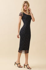 woman wearing a black midi dress with floral print and sheer short sleeves, standing in heels against a neutral background