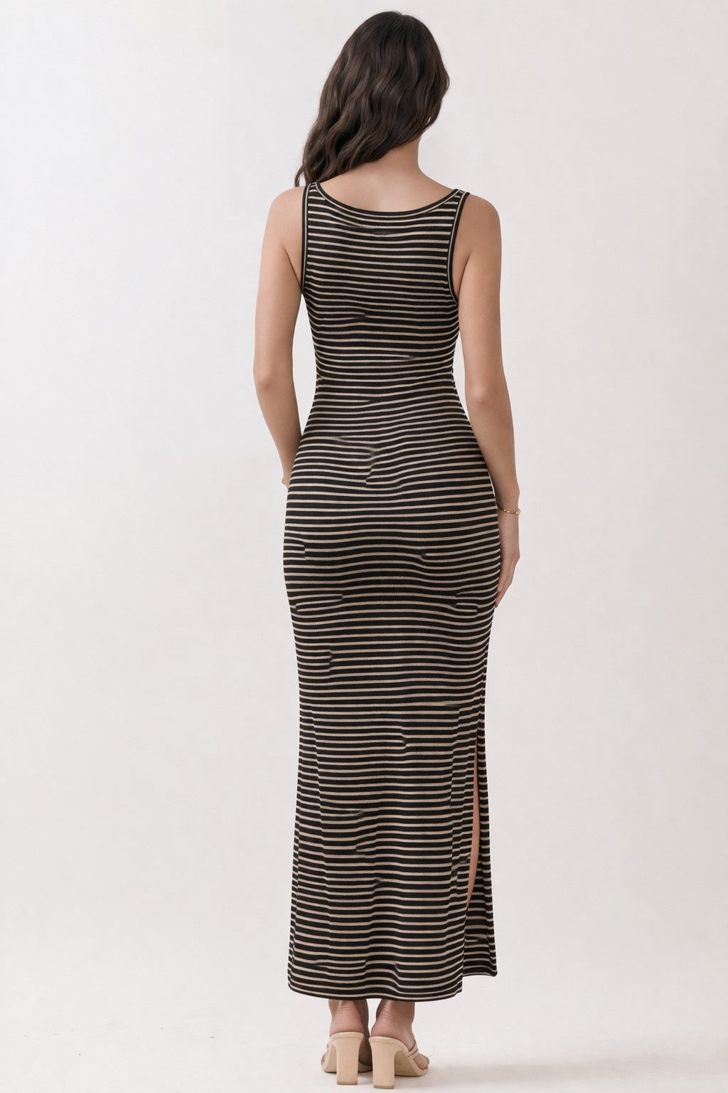 woman wearing a black and tan striped maxi dress with a side slit and a fitted silhouette, seen from the back