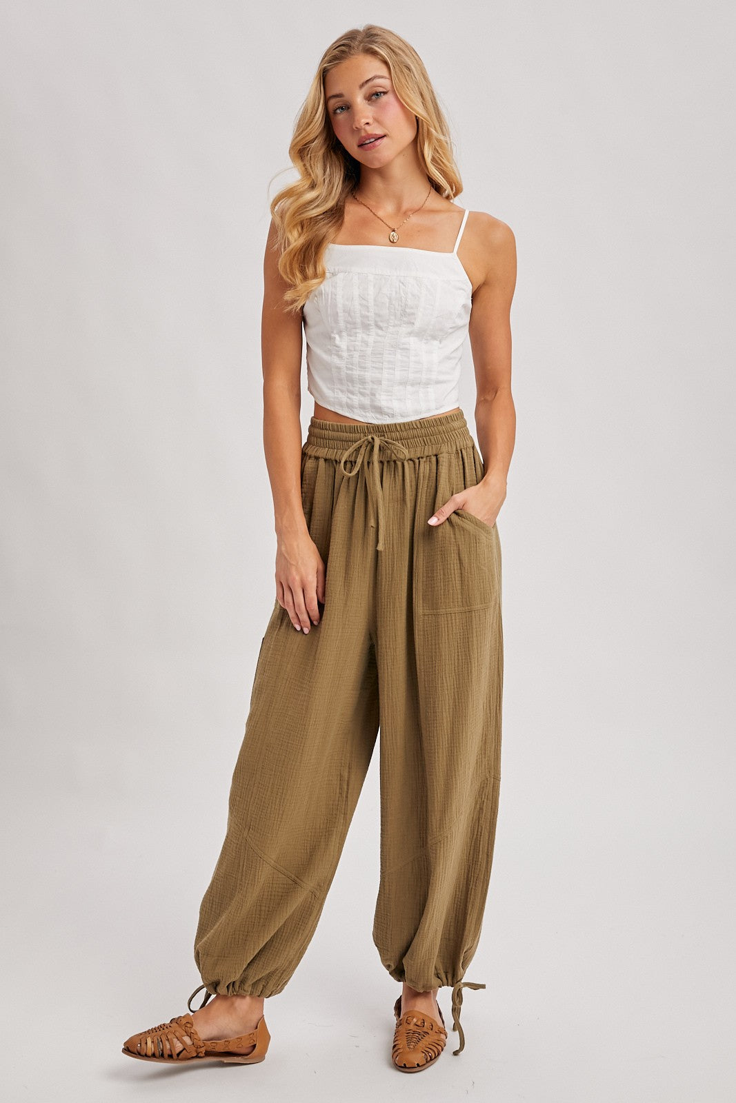 woman wearing a white spaghetti strap top and olive green jogger pants with pockets and drawstring detail