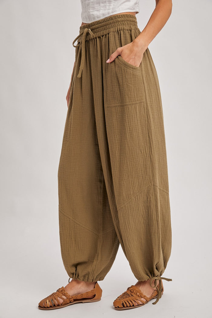 woman wearing olive green loose-fit harem pants with an elastic waistband and pockets, paired with brown strappy sandals