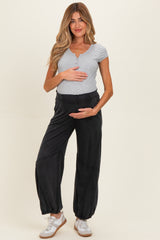 woman wearing a gray short sleeve maternity top and black jogger pants, holding her baby bump