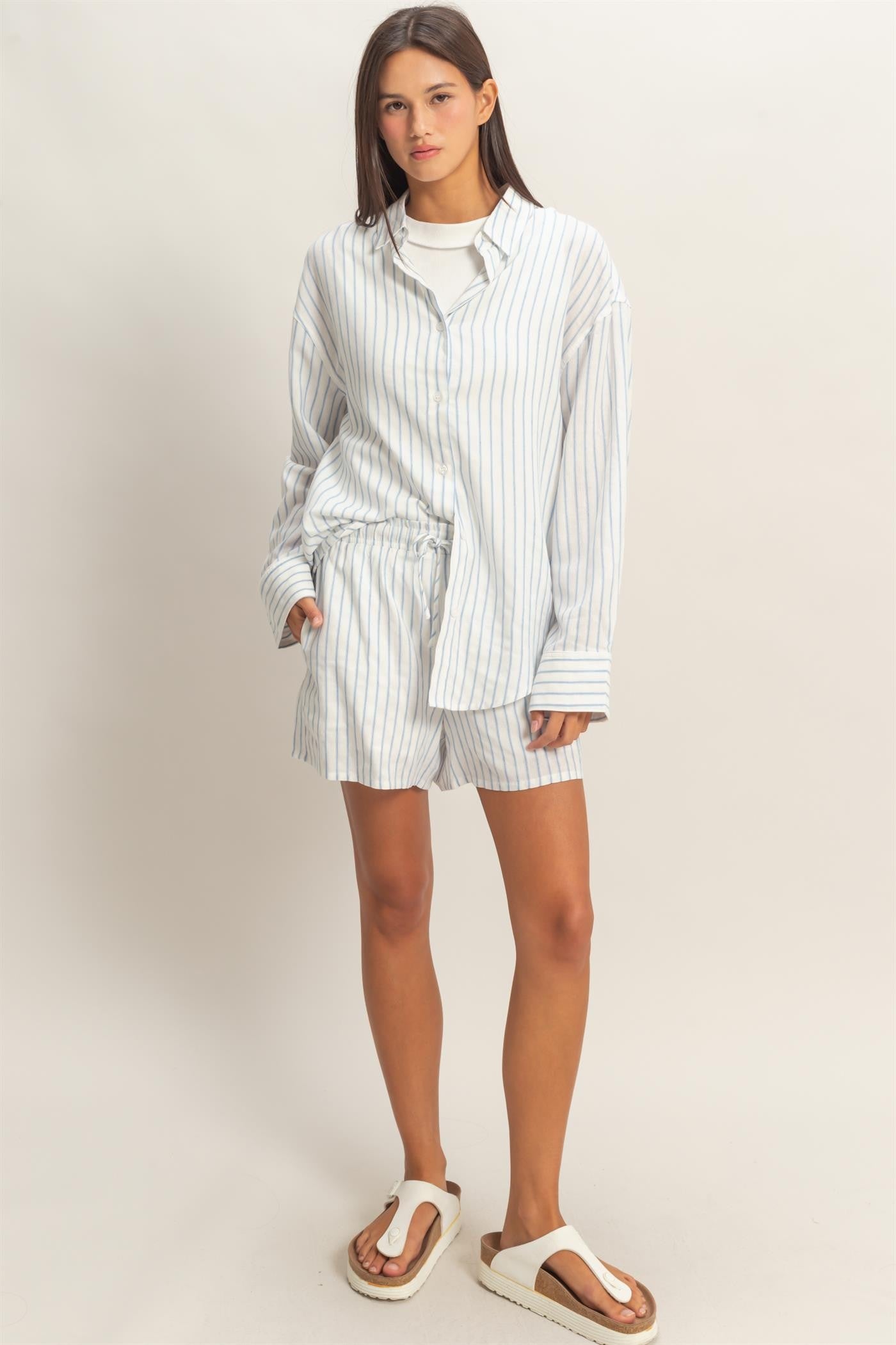 woman wearing a white and light blue striped oversized shirt and matching shorts with flip-flops