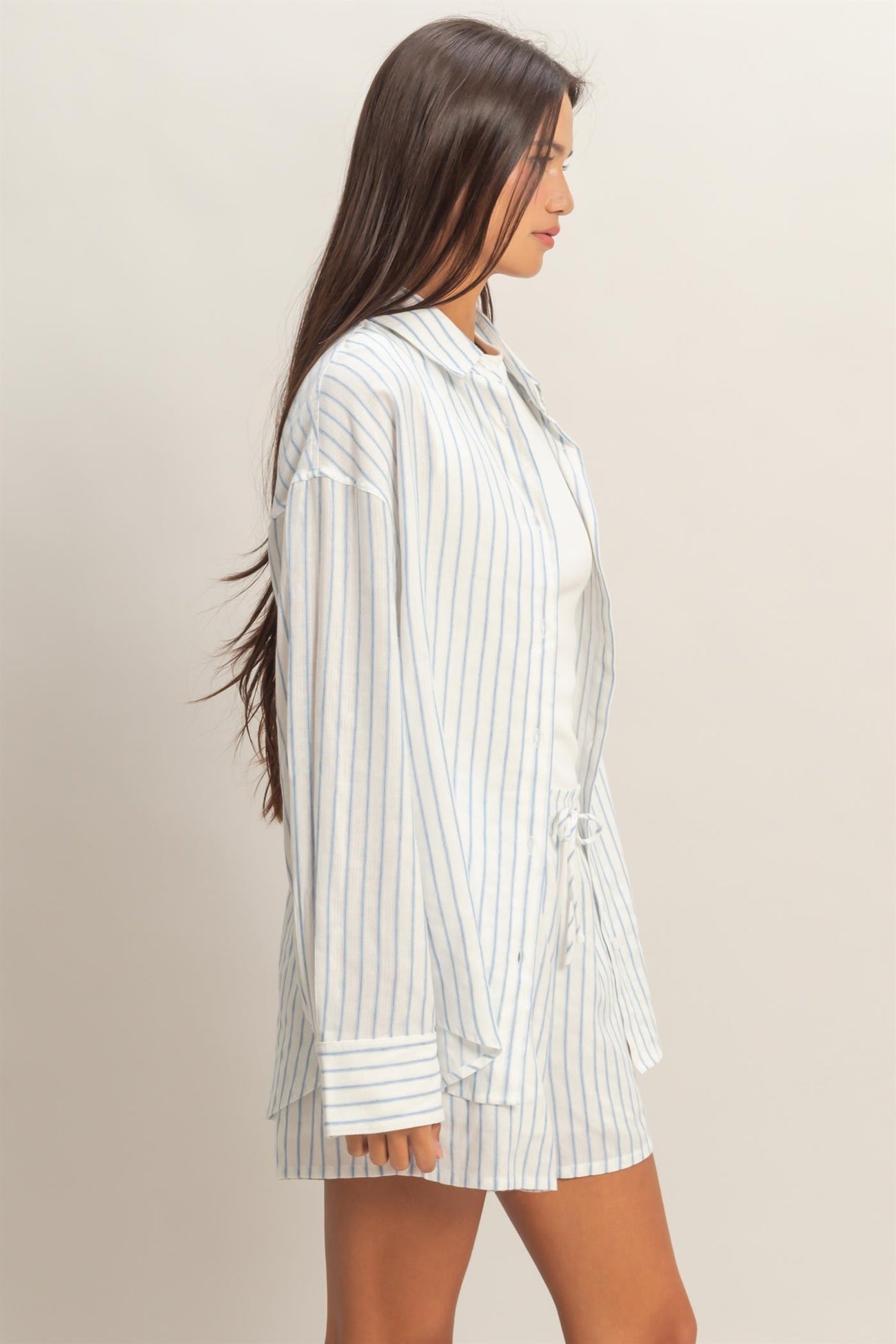 woman wearing a white and blue striped oversized shirt with a drawstring waist and a light tank top underneath