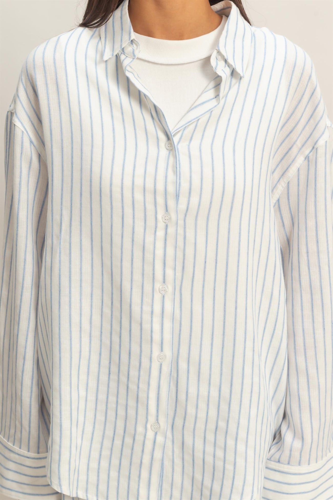 woman wearing a white and light blue striped button-up shirt over a white long sleeve top