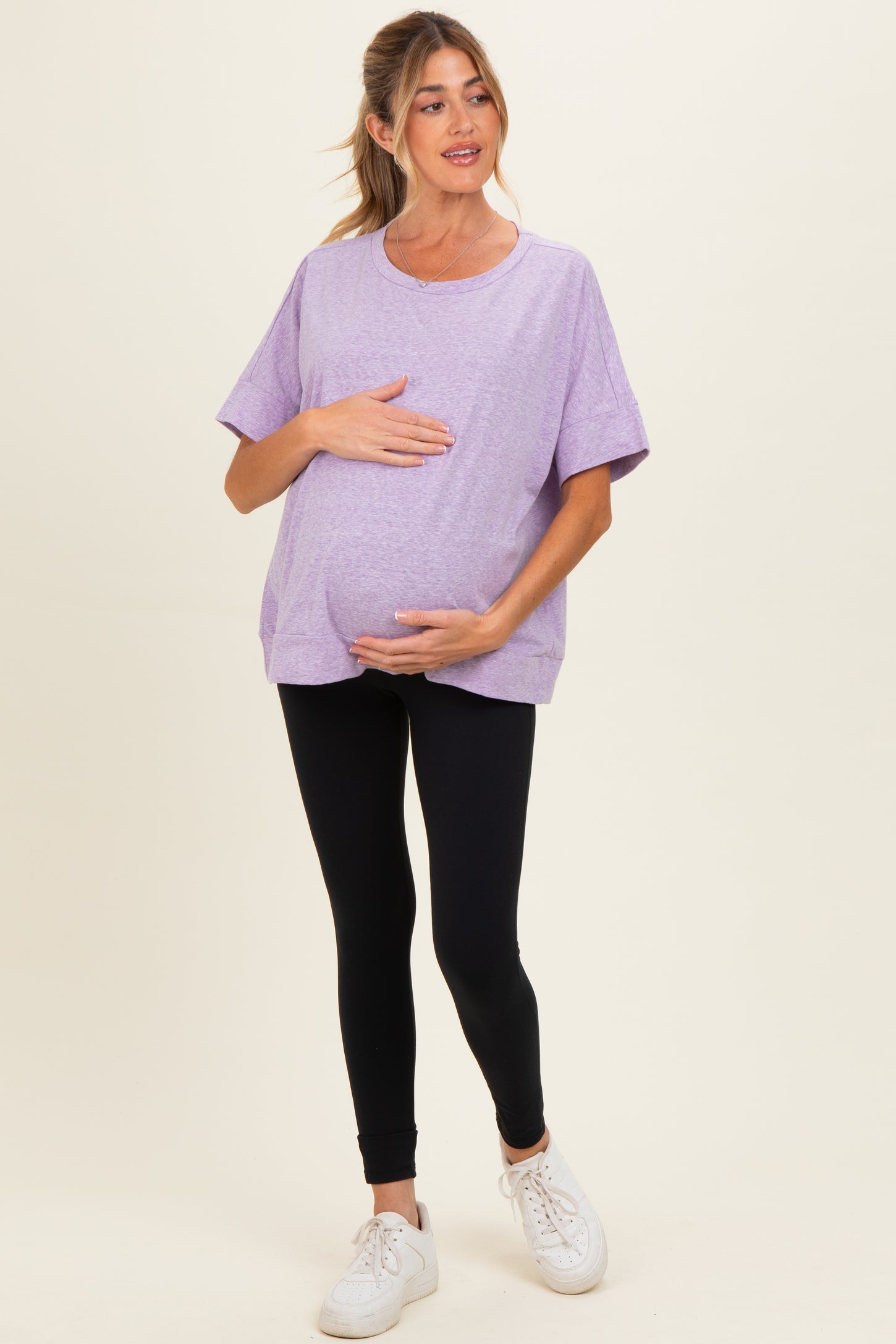 woman wearing a purple oversized maternity t-shirt and black leggings, holding her baby bump