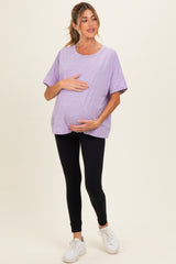 woman wearing a purple oversized maternity t-shirt and black leggings, holding her baby bump