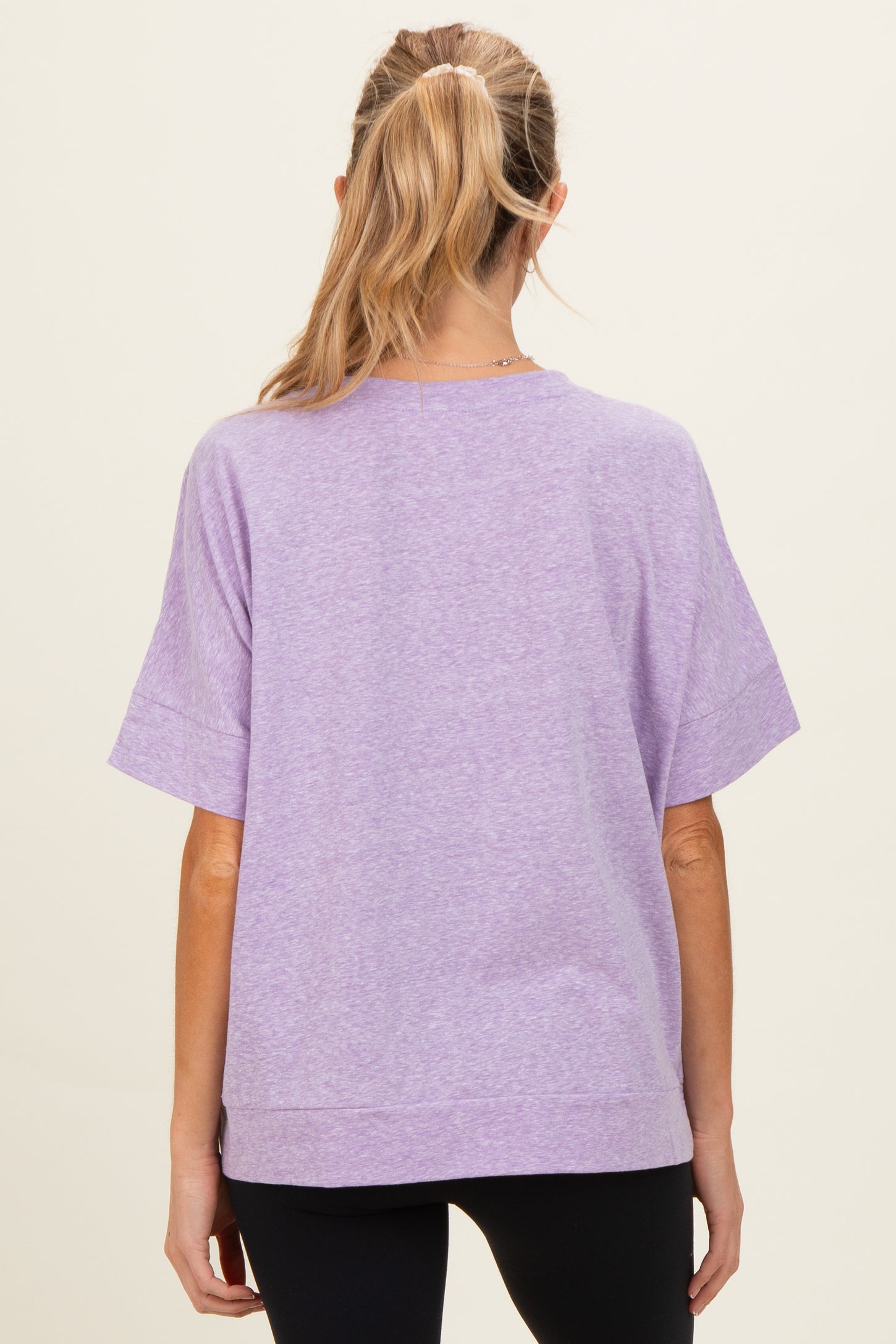 woman wearing a lavender short sleeve maternity top, viewed from the back with a relaxed fit and side slits
