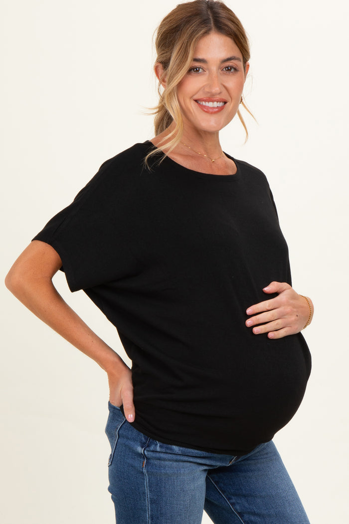 woman wearing a black maternity top and holding her baby bump while smiling