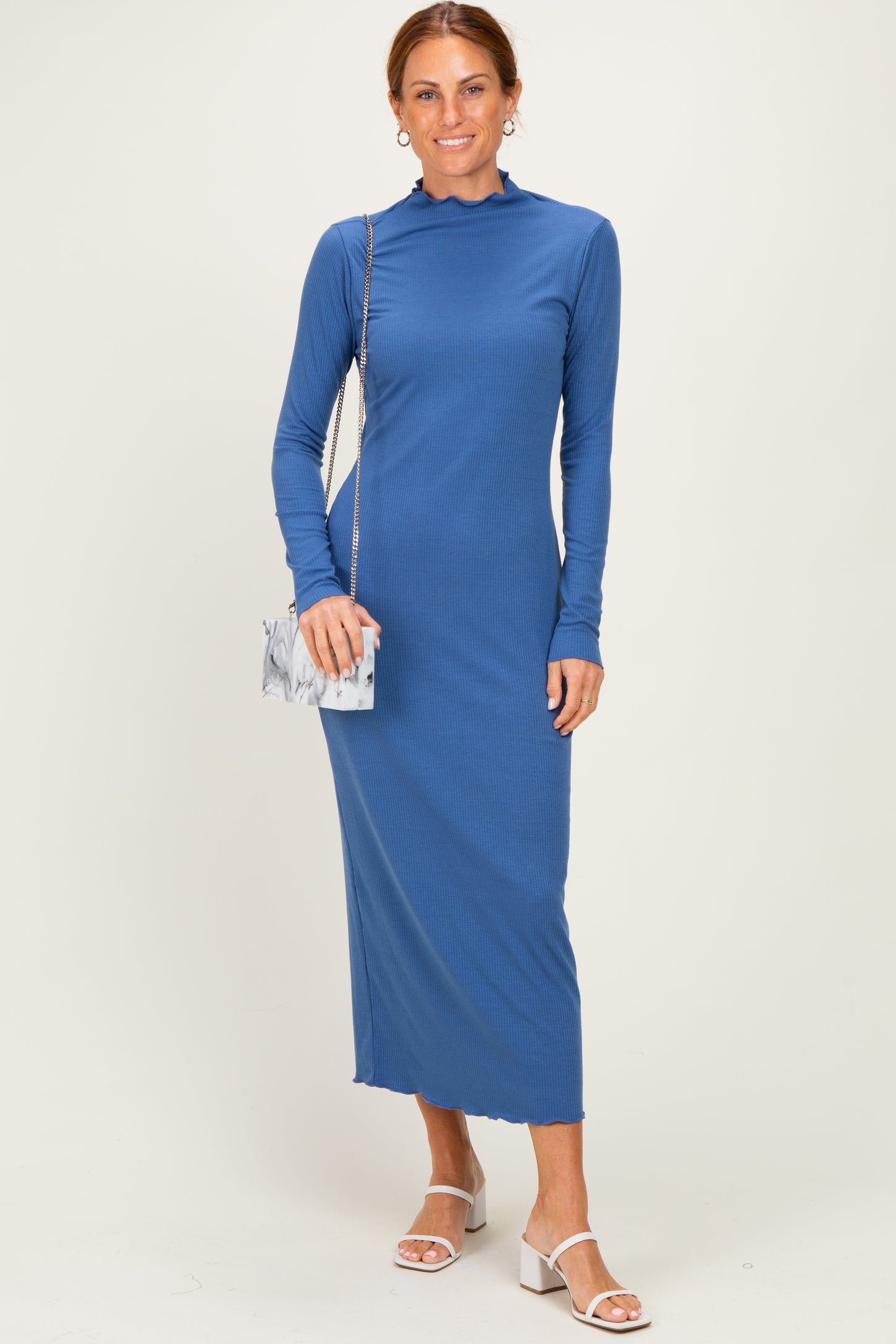 woman wearing a blue long sleeve ribbed maxi dress with a high neck and holding a marble clutch bag