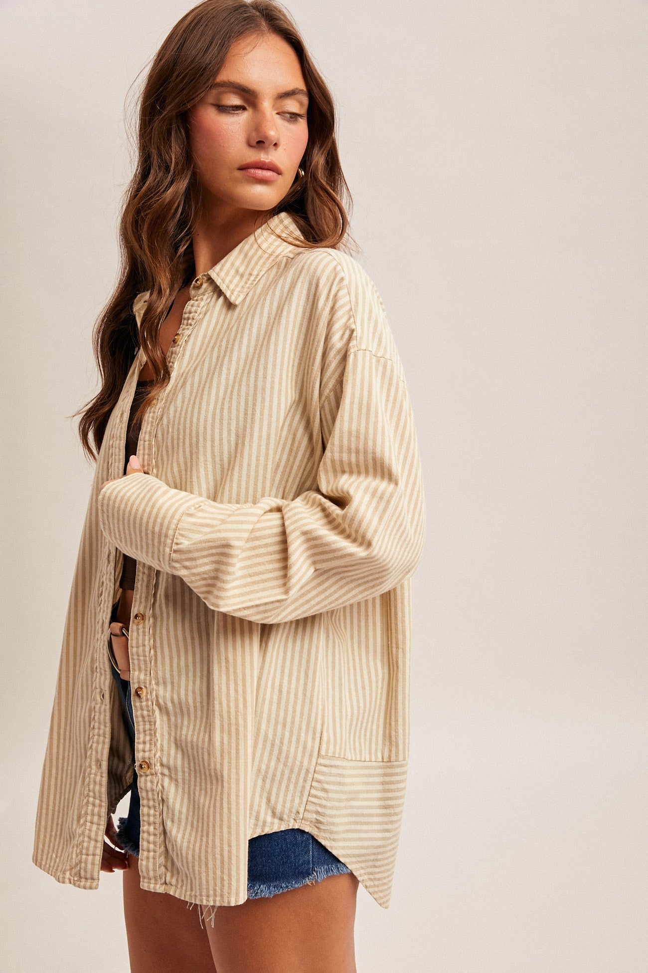 woman wearing a beige and cream striped oversized shirt with button details, paired with denim shorts