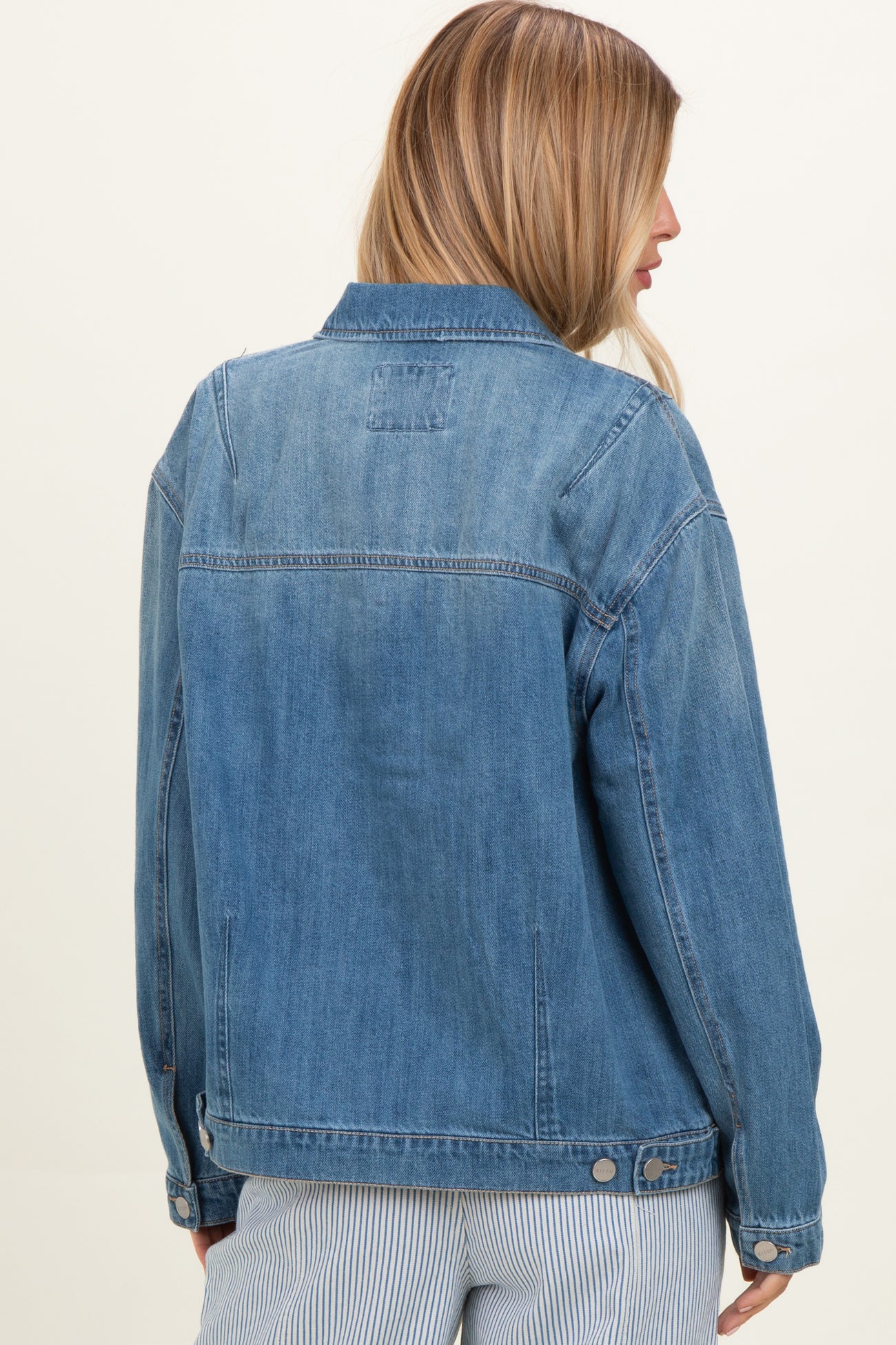 woman wearing a light blue denim jacket, viewed from the back, with a relaxed fit and classic style details