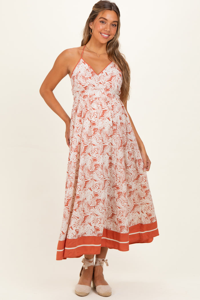 woman wearing a floral maternity maxi dress with a v-neck and halter straps, featuring a tiered skirt and an empire waist
