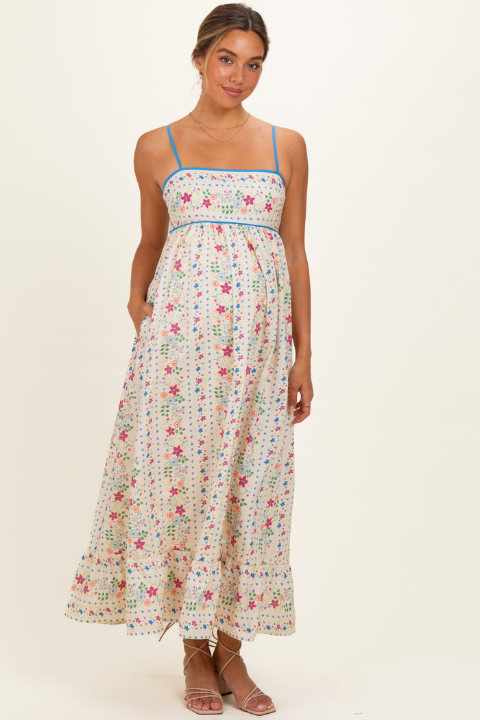 woman wearing a floral print maternity maxi dress with blue straps and pockets, showcasing her baby bump