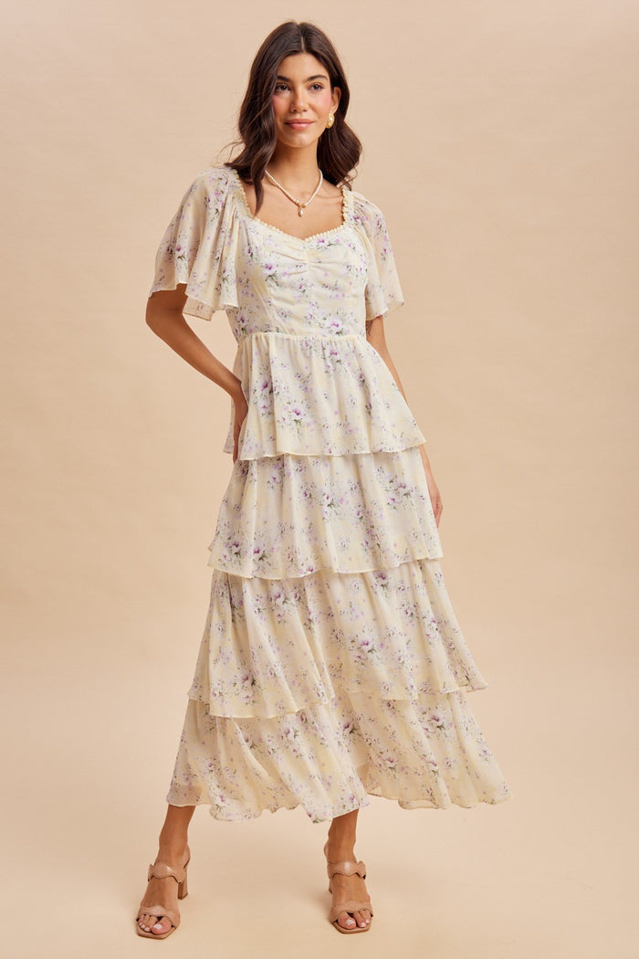 woman wearing a cream floral maxi dress with tiered layers and flutter sleeves