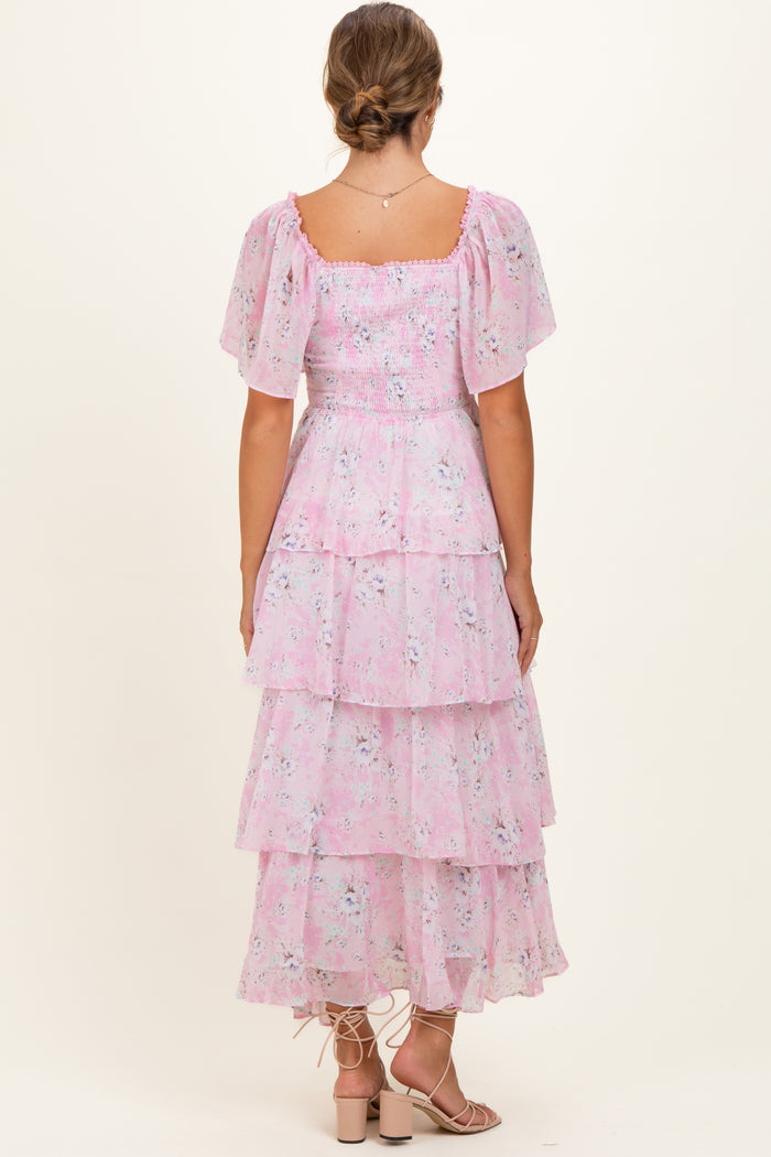 woman wearing a pink floral maternity dress with tiered ruffles and short puff sleeves, viewed from the back