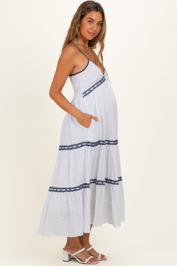woman wearing a white and navy polka dot maternity maxi dress with spaghetti straps and pockets, showing her baby bump