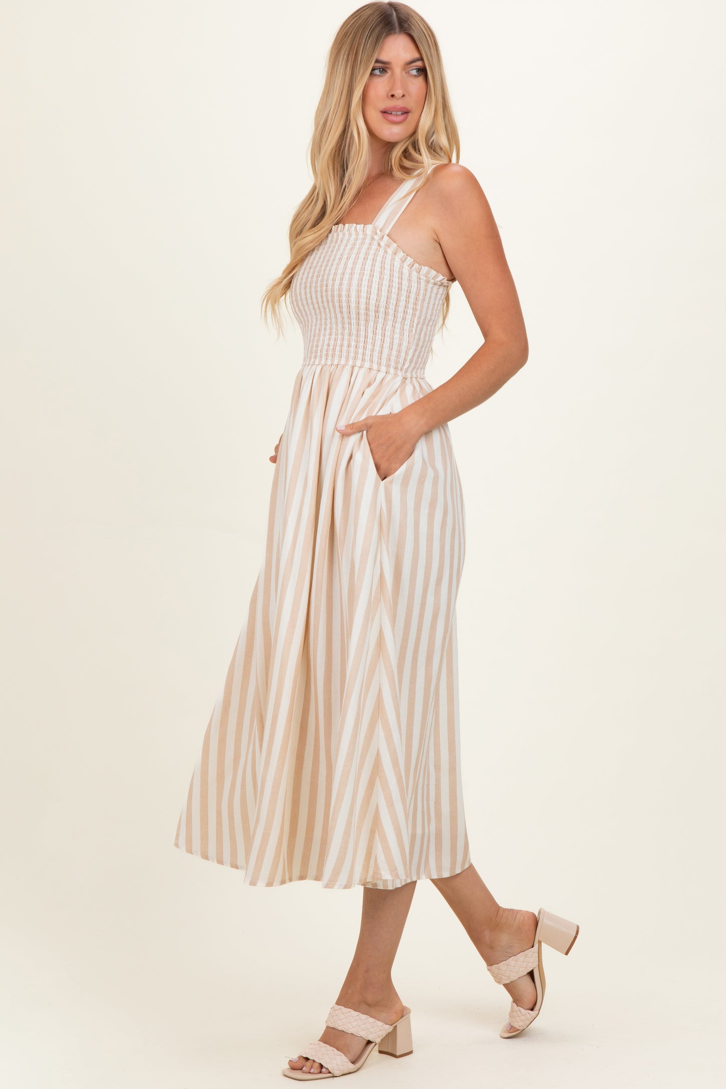 woman wearing a cream and beige striped midi dress with a smocked bodice and pockets, styled with heeled sandals