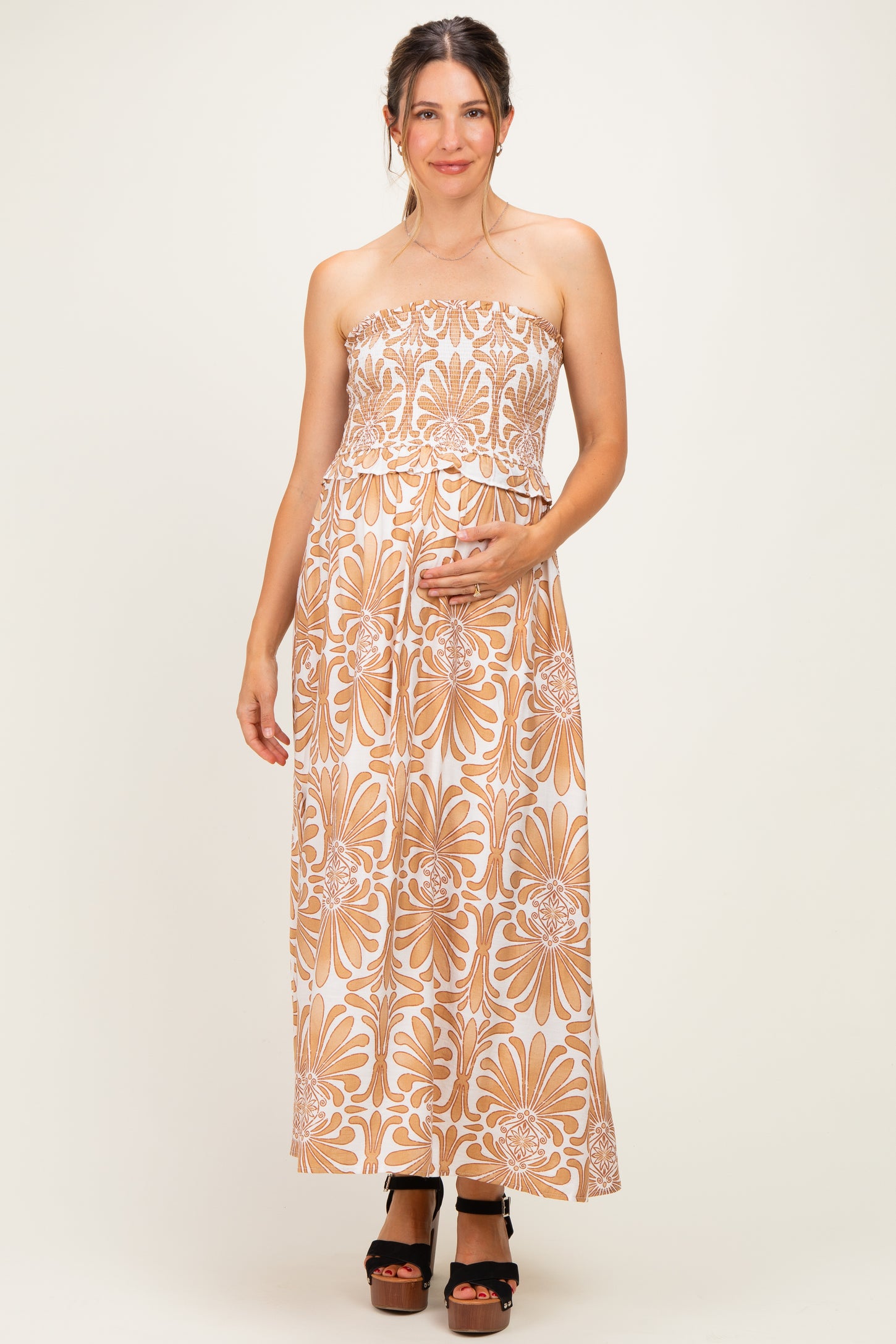 woman wearing a strapless beige floral maternity maxi dress and holding her baby bump