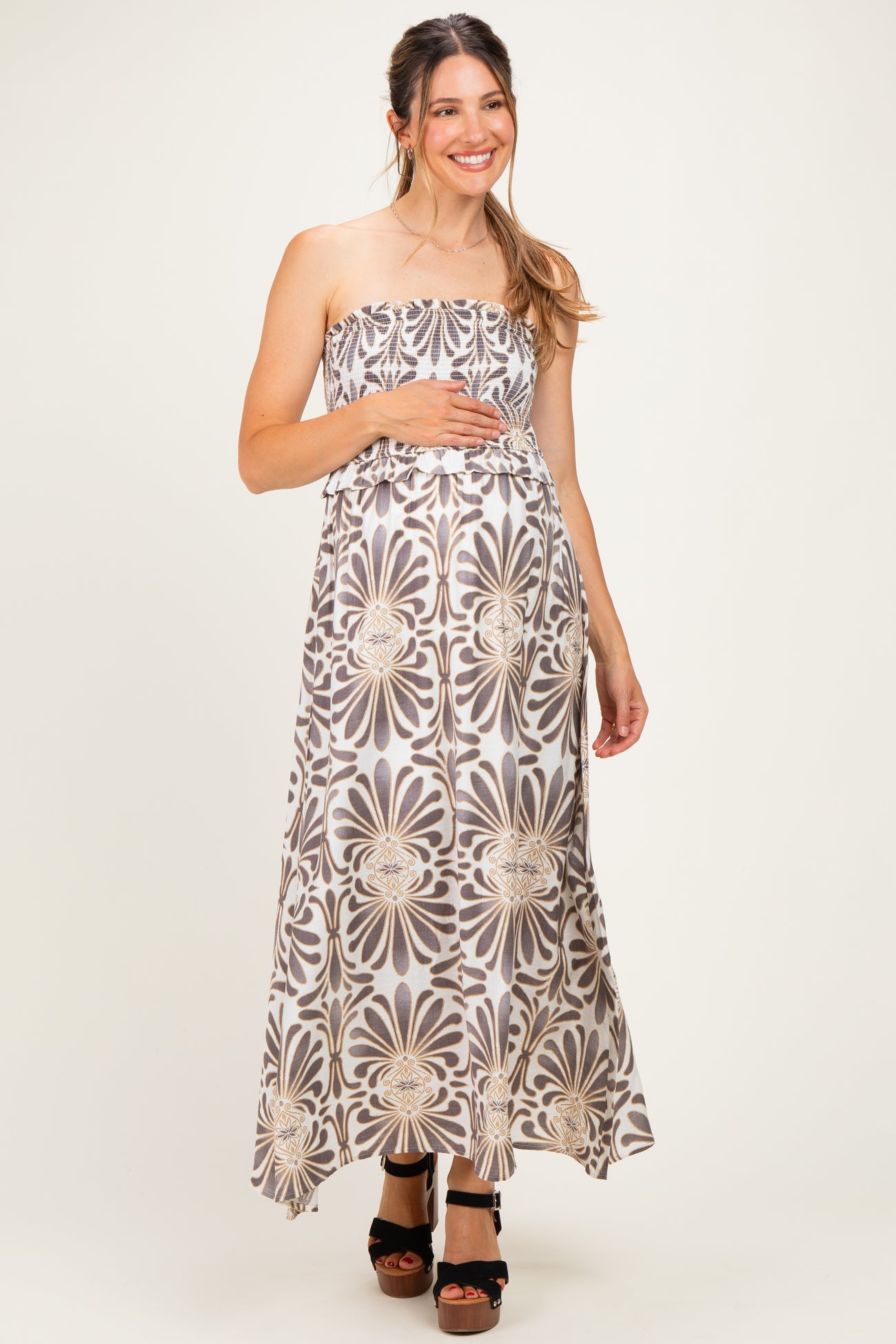 woman wearing a strapless floral maxi maternity dress and holding her baby bump