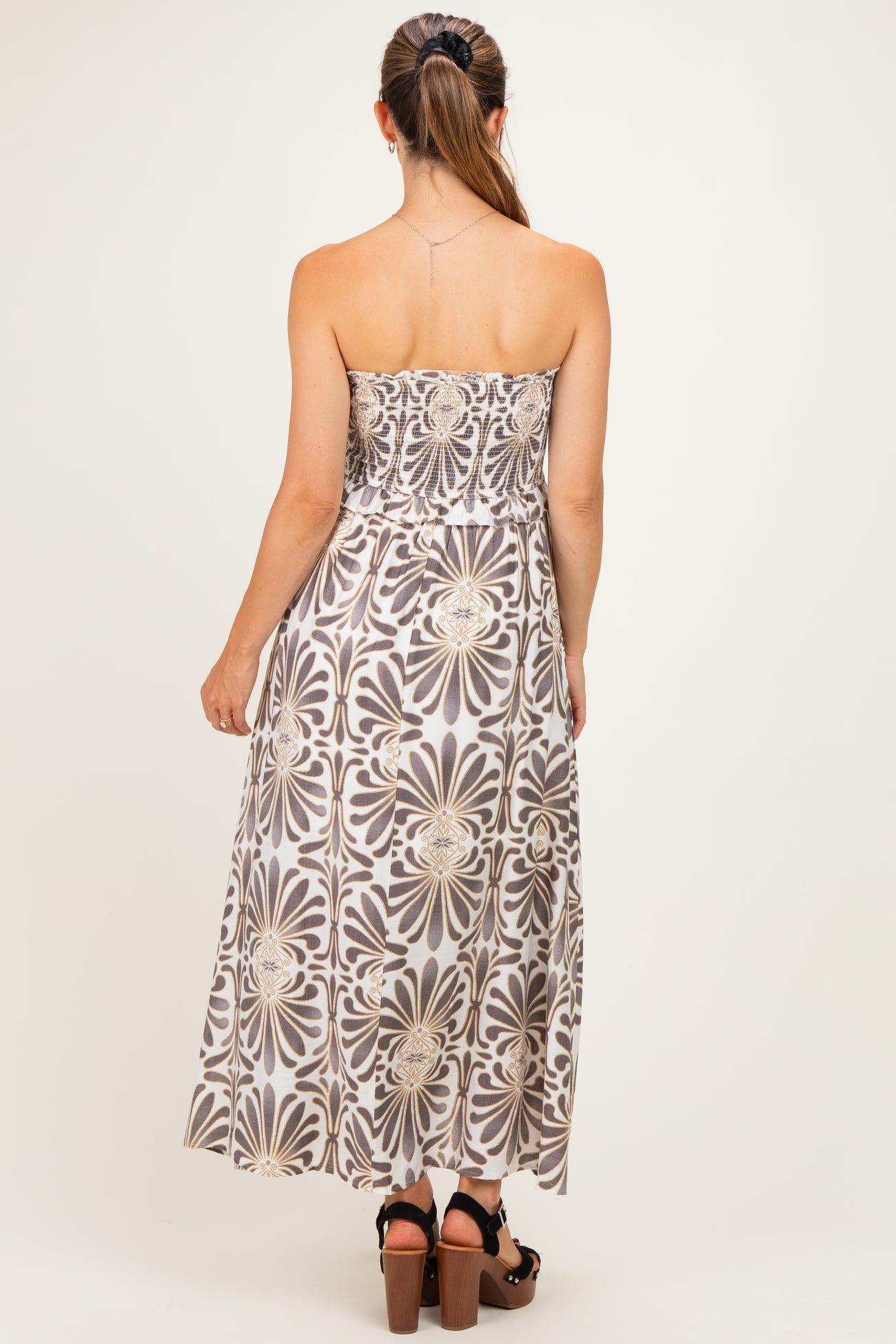 woman wearing a strapless floral maternity maxi dress with a fitted bodice and flowing skirt, showing her back