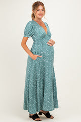 woman wearing a green maternity maxi dress with short puff sleeves and pockets, gently cradling her baby bump