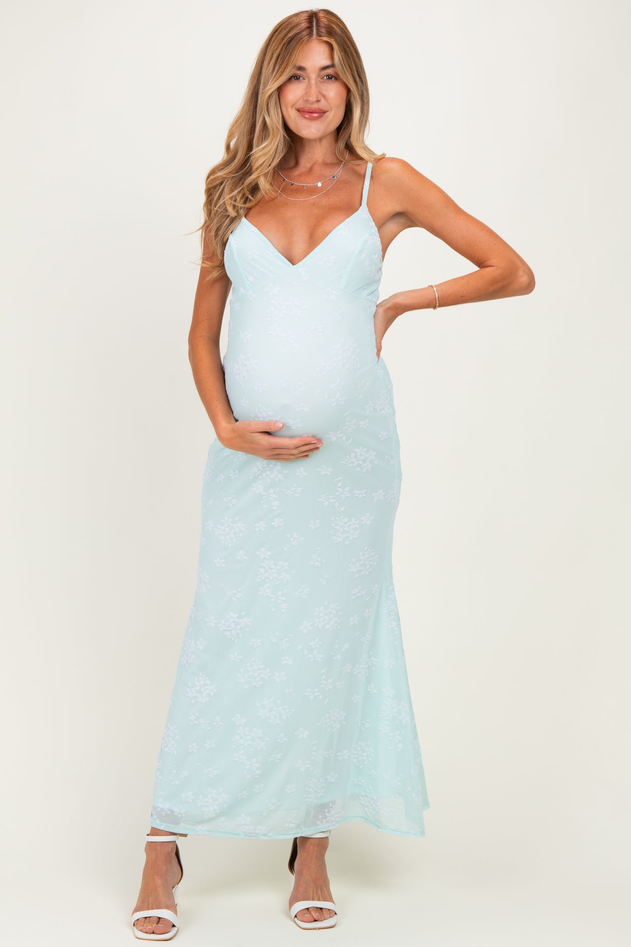 woman wearing a light mint green floral maternity dress with spaghetti straps and a visible baby bump