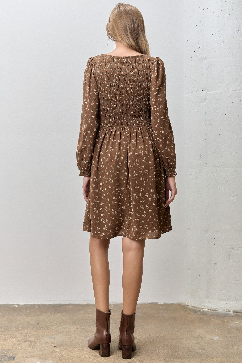 woman wearing a brown floral smocked mini dress with long sleeves and a slight flare at the hem