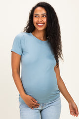 woman wearing a light blue short sleeve maternity top and holding her baby bump